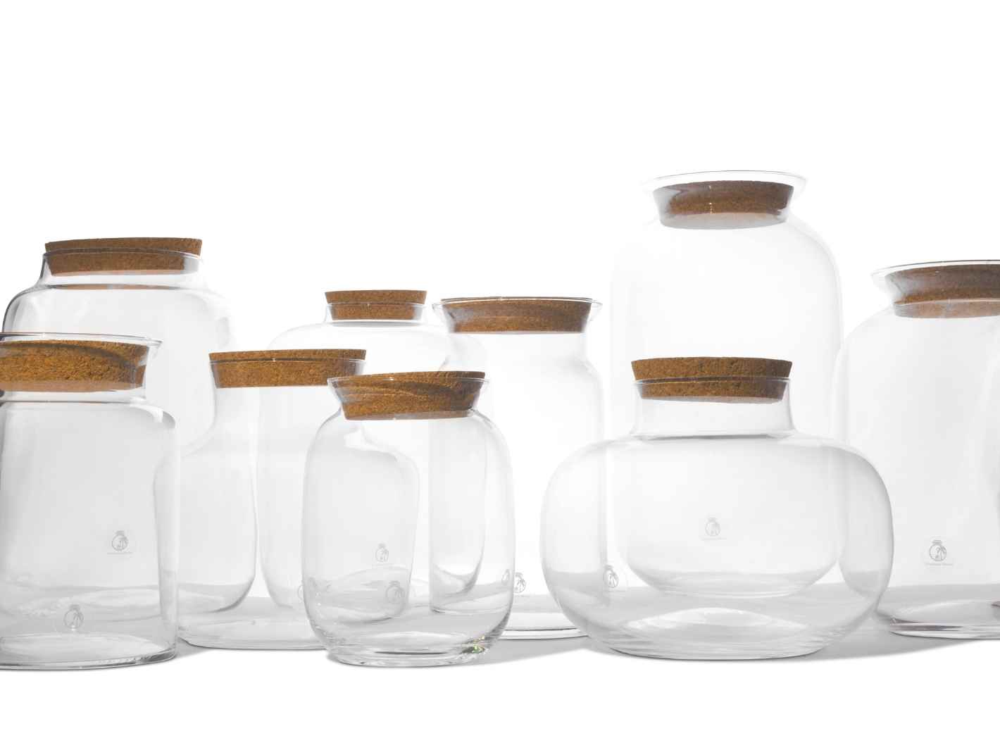 A collection of clear glass containers of various sizes is displayed, each featuring a cork lid. The glass has a smooth finish, and the lids are neatly placed on top, showcasing their simple yet elegant design.
