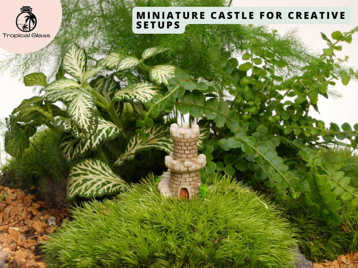 Mini mossy fairy castle figurine placed inside a terrarium with moss, stones and tiny plants