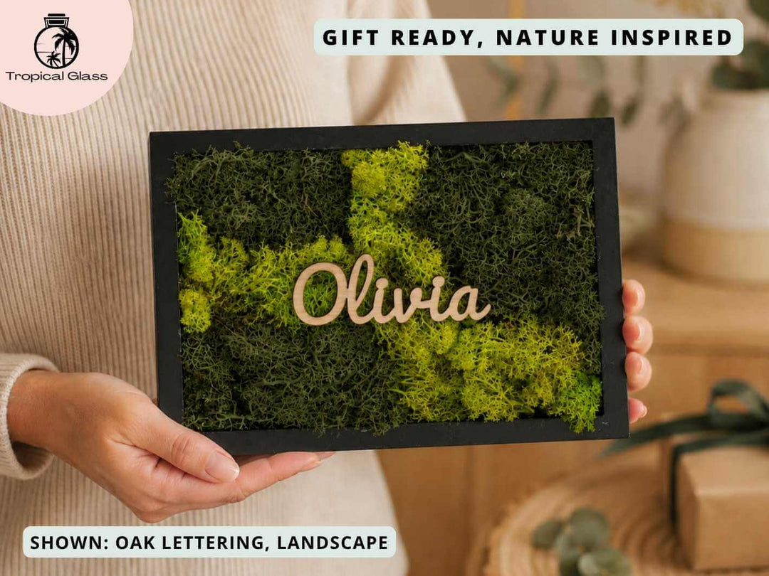 A person holds a personalised moss wall art frame featuring vibrant green preserved moss and the name Olivia in elegant wooden lettering.