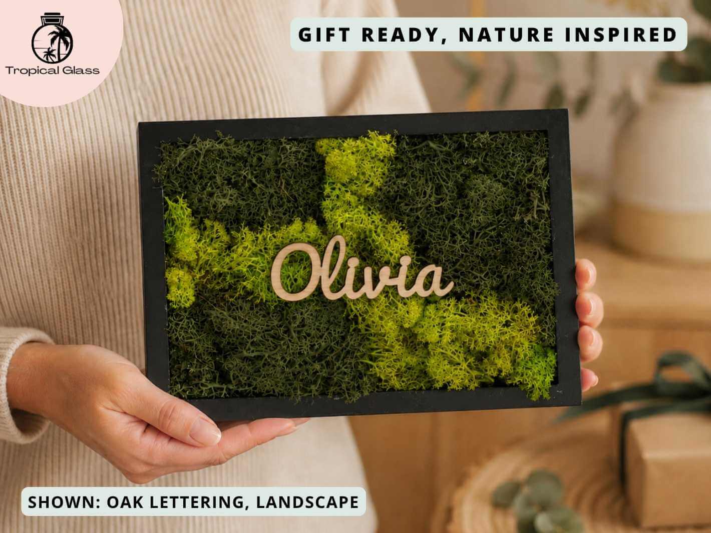A person holds a personalised moss wall art frame featuring vibrant green preserved moss and the name Olivia in elegant wooden lettering.