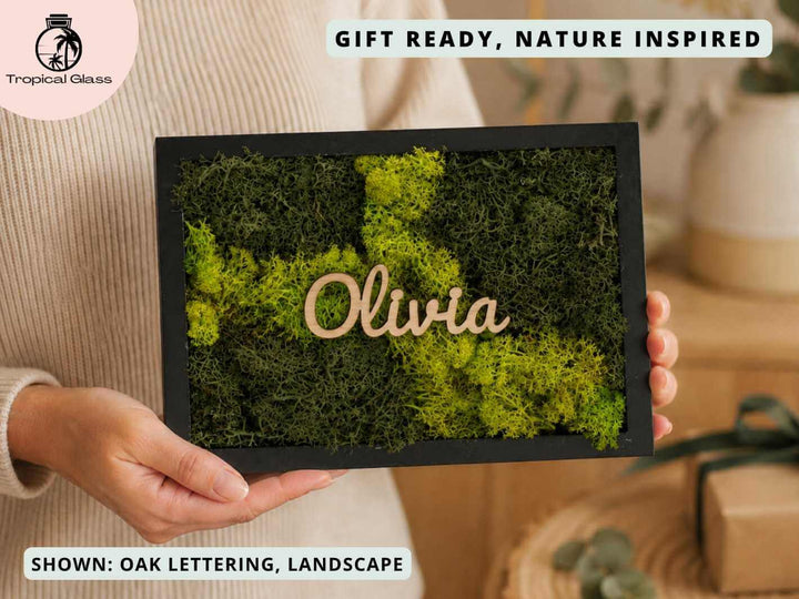 A person holds a personalised moss wall art frame featuring vibrant green preserved moss and the name Olivia in elegant wooden lettering.