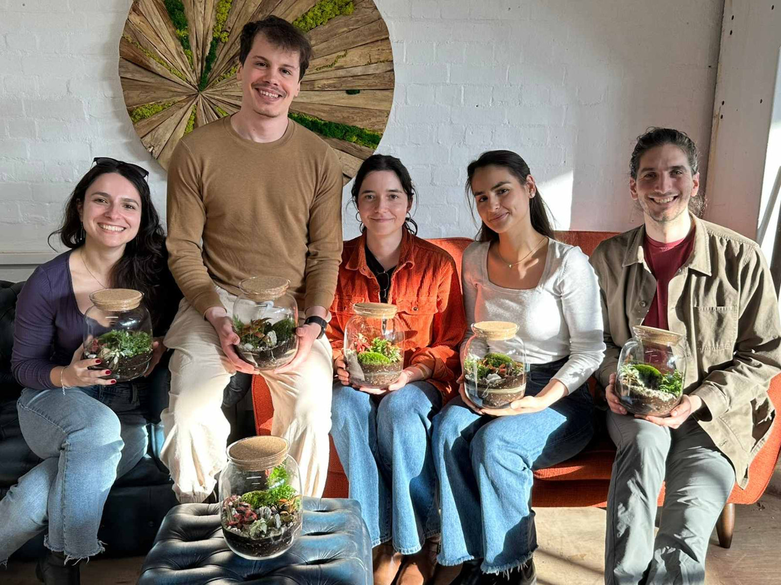 Five people sitting together holding small terrariums in a casual indoor setting.