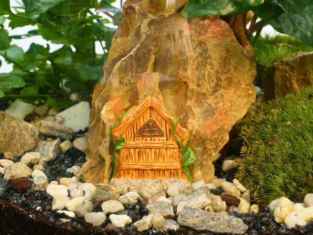 Miniature wooden fairy house inside a terrarium with moss, rocks, and pebbles