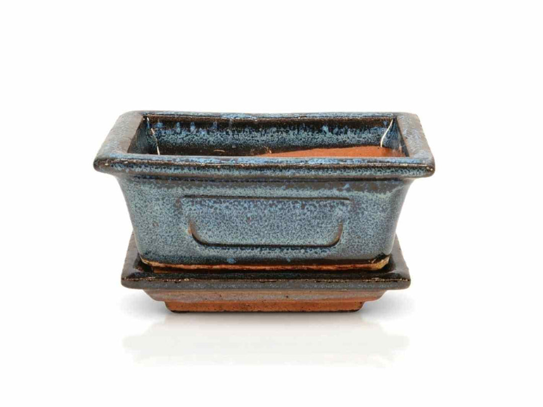 A rectangular decorative pot with a dark blue glazed finish sits atop a matching saucer. The pot features a sleek design.