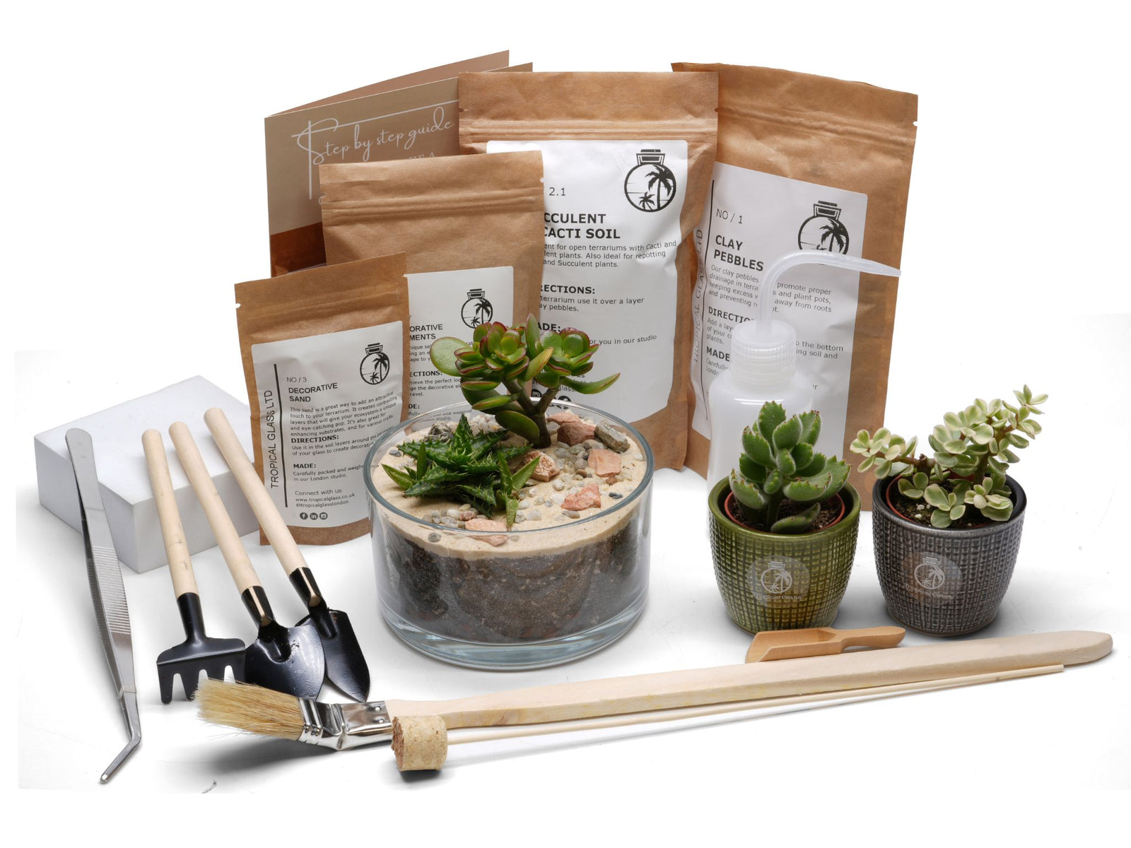 A DIY Open Terrarium Kit is displayed, featuring a glass container filled with soil, decorative stones, and two succulent plants. The kit includes various tools, soil bags, and instructions, all neatly arranged for easy assembly.