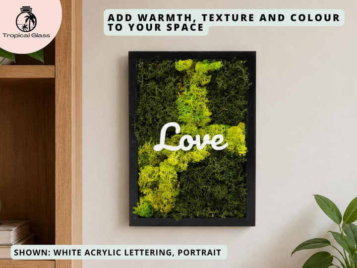 A framed piece of preserved moss art featuring bright green and yellow moss arranged in a decorative pattern. The word Love is prominently displayed in white acrylic lettering, adding a warm and inviting touch to the space.