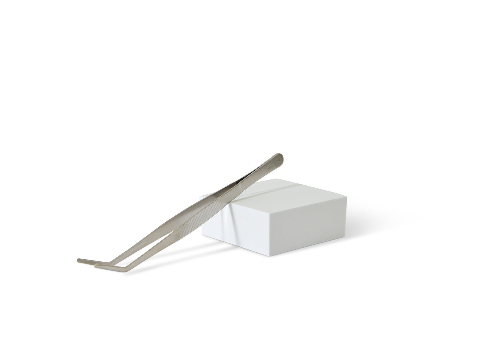 A pair of curved terrarium tweezers rests on a white rectangular box. The tweezers feature a sleek metallic finish and are designed for precision in arranging plants and decorative items in terrariums.