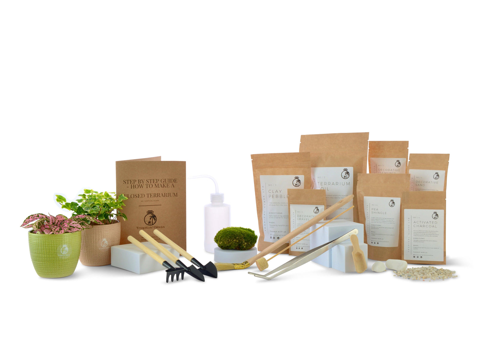 A DIY terrarium starter kit displayed on a white background, featuring tools, soil, and decorative elements like moss and rocks.