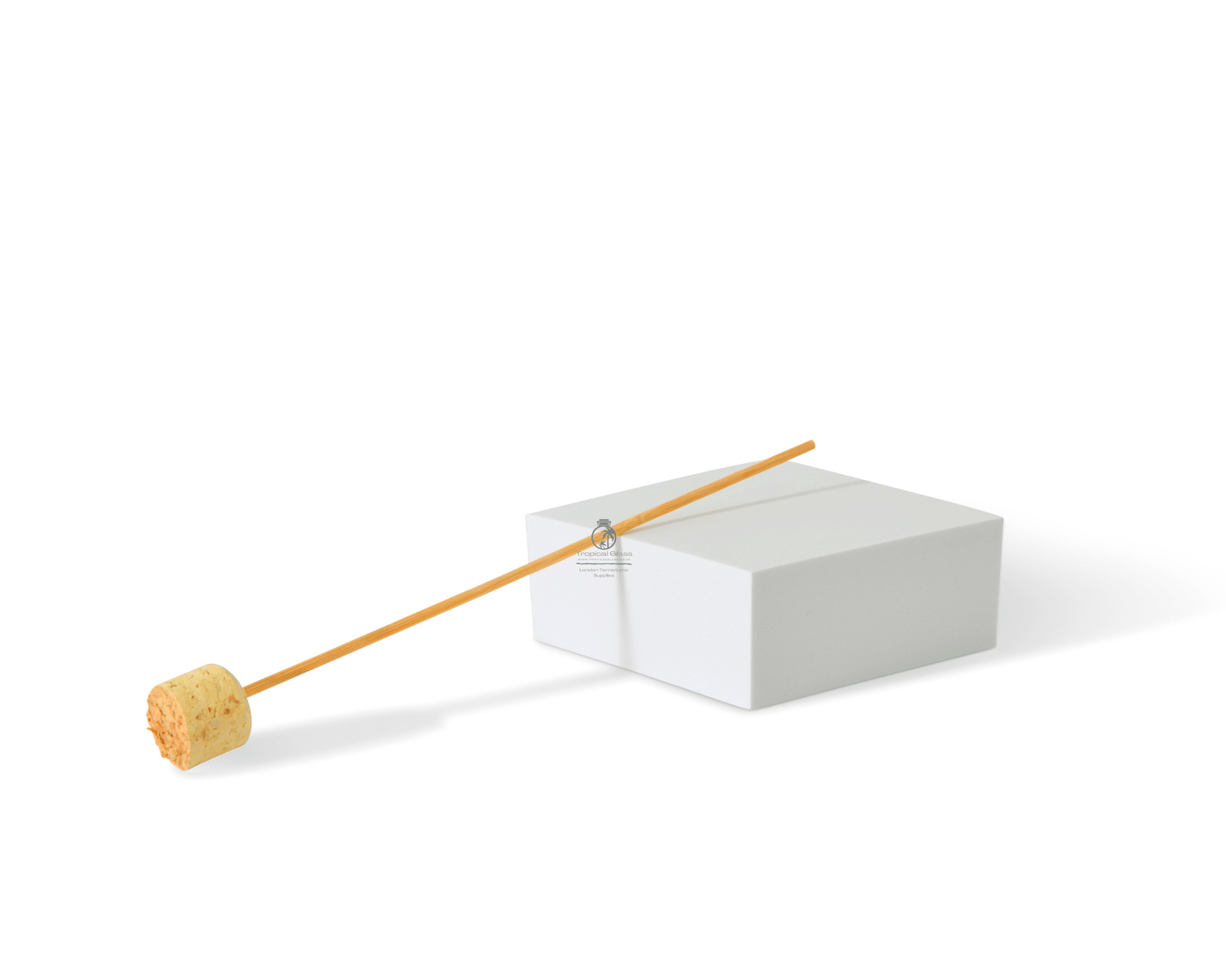 A natural cork tamper rests on a white surface beside a rectangular white block. The tamper features a cylindrical cork head attached to a long wooden stick, ideal for pressing down soil and plants in terrarium setups.