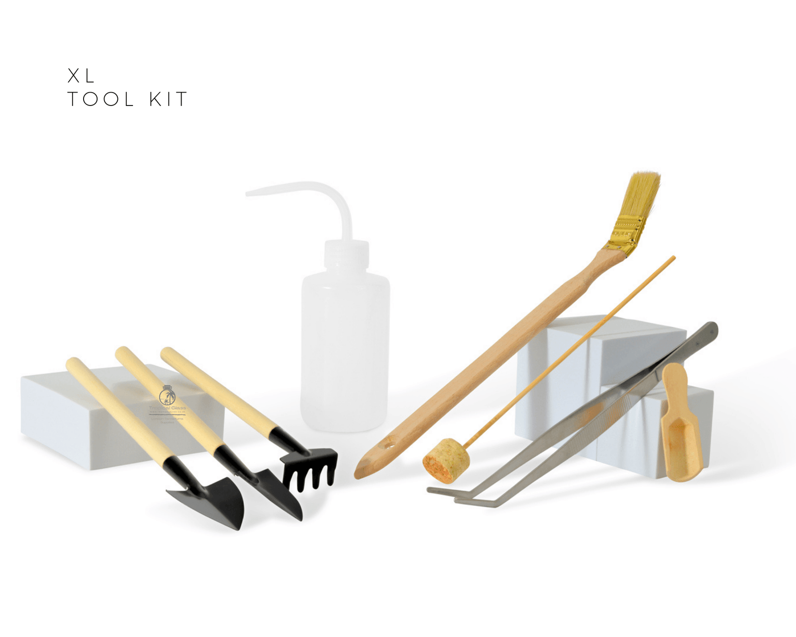 An XL garden tool kit featuring eight pieces, including a shovel, rake, spade, brush, cork tamper, watering bottle, wooden spoon, and tweezers, displayed alongside white boxes.