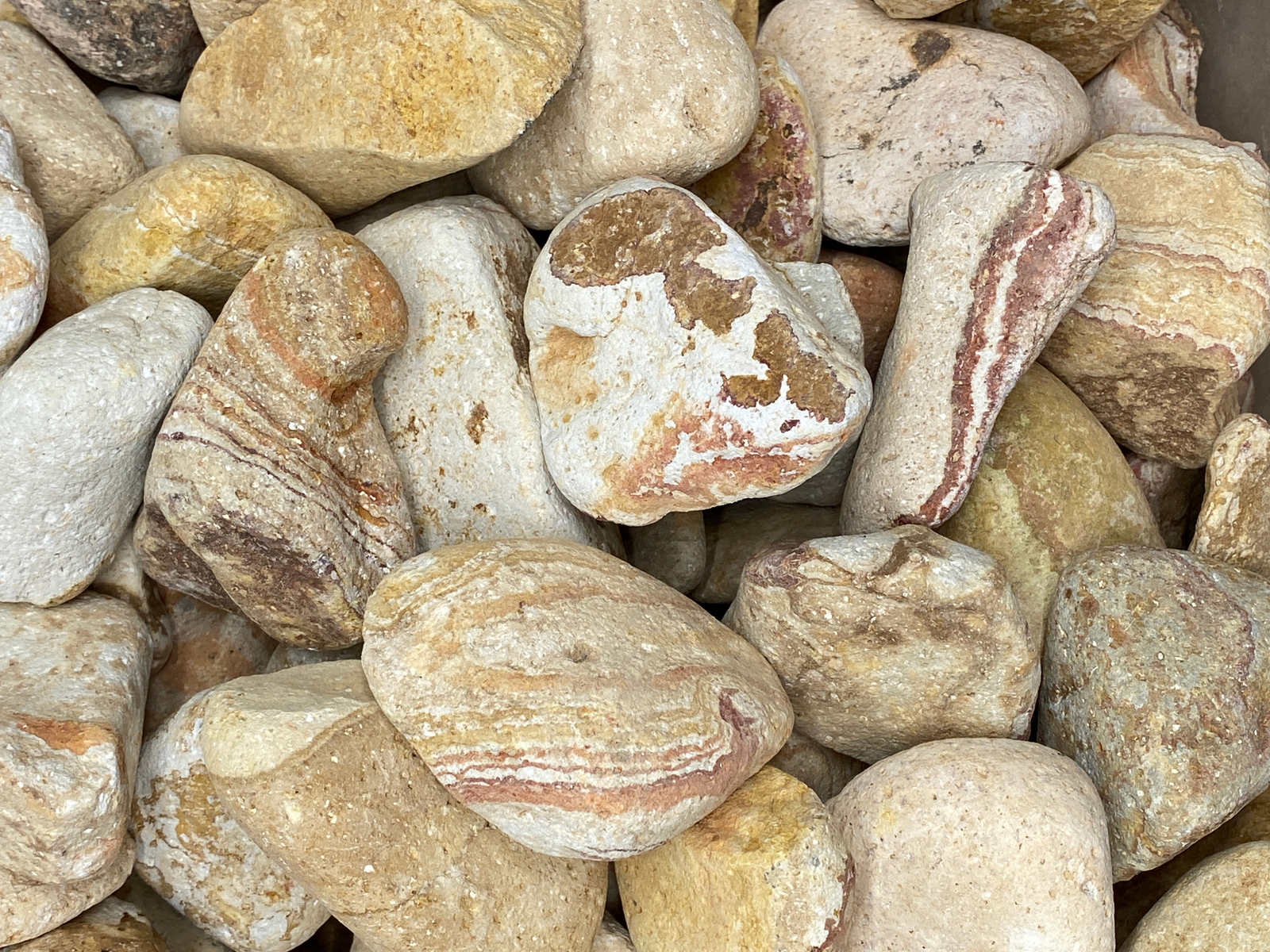 A close-up view of various natural stones featuring a mix of beige, cream, and orange hues with distinctive marble patterns. The stones vary in size and shape, creating an appealing texture perfect for decorative purposes.