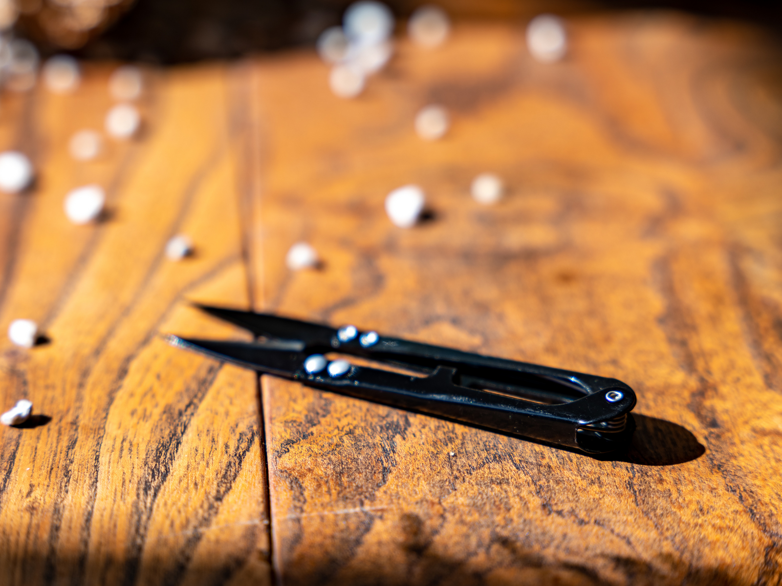 A pair of sleek black pruning snips is displayed on a textured wooden surface, surrounded by small white pebbles. The snips feature a compact design, ideal for delicate plant trimming tasks.