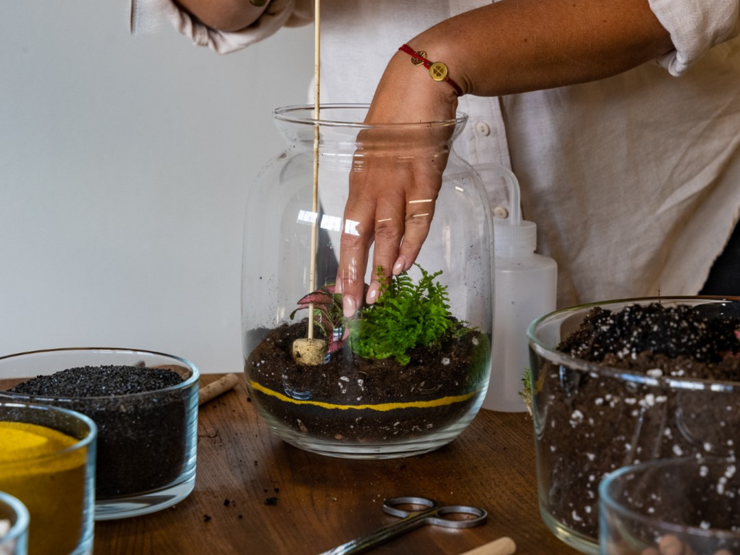 A woman is using a Tropical Glass Cork Tamper to put plants in a vase.