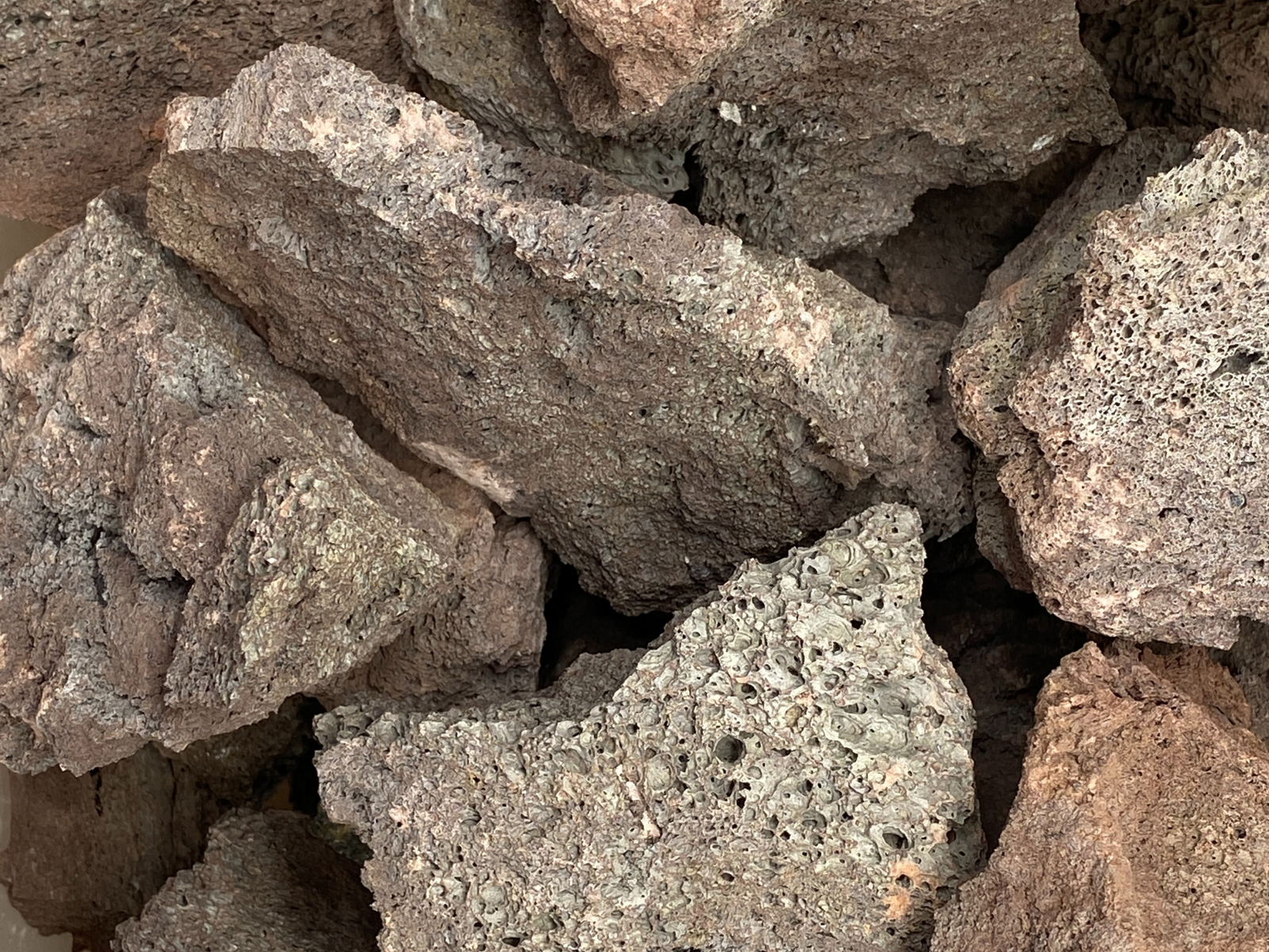 A close-up view of several dark, rugged lava rock stones stacked together, showcasing their porous texture and irregular shapes.